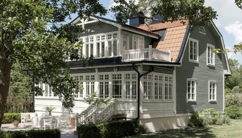 Vackert putsade hus med gröna träfasader och vita detaljer. En veranda med vita möbler och en uteplats inbjuder till avkoppling. Perfekt inspiration för putsade hus.