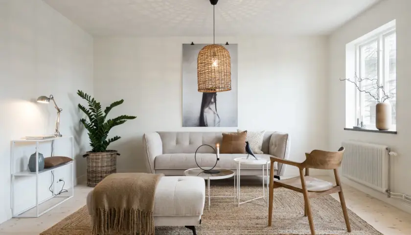 Mysigt vardagsrum i ett tidstypiskt 30-talshus med bekväm soffa, jutematta och en vacker rottinglampa som sprider ett varmt ljus.