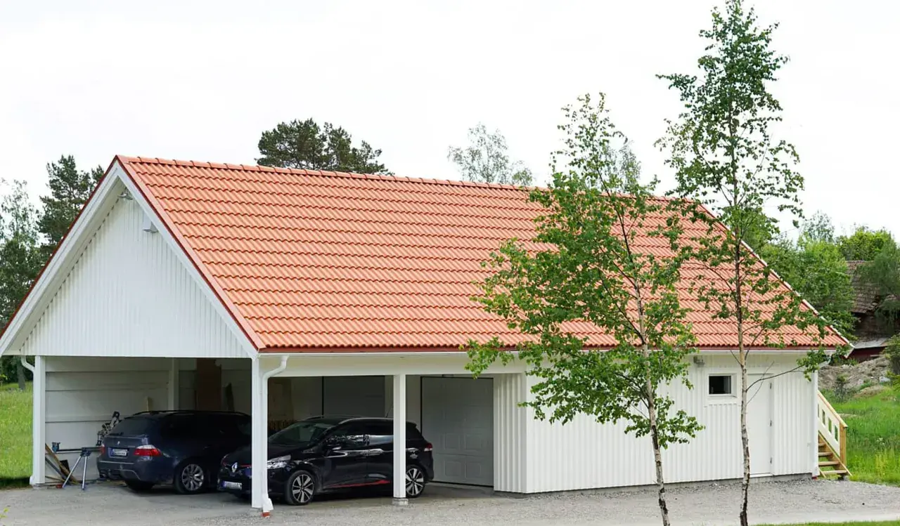 Ett vitt hus med tegeltak, där en del är en carport med två bilar och en annan del är ett garage. Kanske en ombyggnad för att bygga om carport till garage.