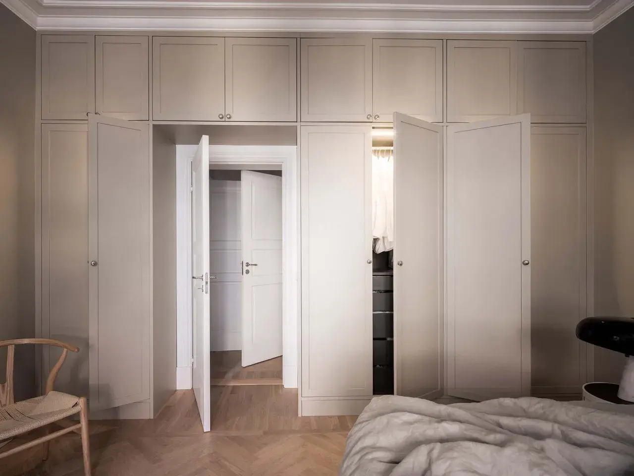 En elegant garderob i sekelskiftesstil med ljusa fronter och dörrar som leder till en walk-in closet.