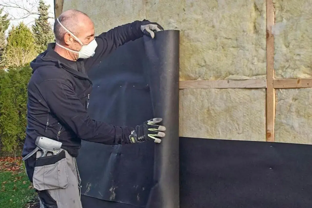 Man med mask rullar ut vindpapp på insidan av en isolerad vägg.