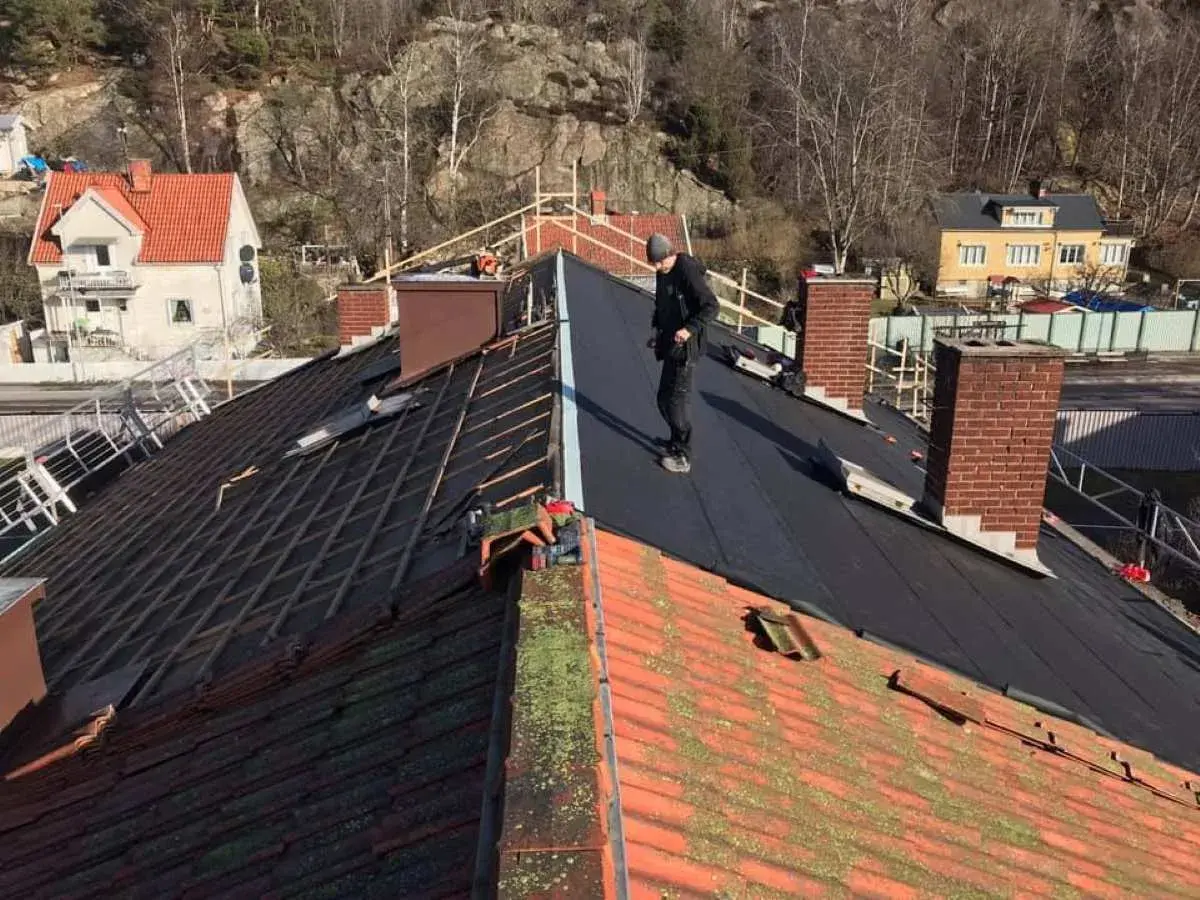Takläggare arbetar på ett tak där gamla tegelpannor byts ut mot nytt material. Kanske funderar de på aluzink nackdelar inför framtida projekt.