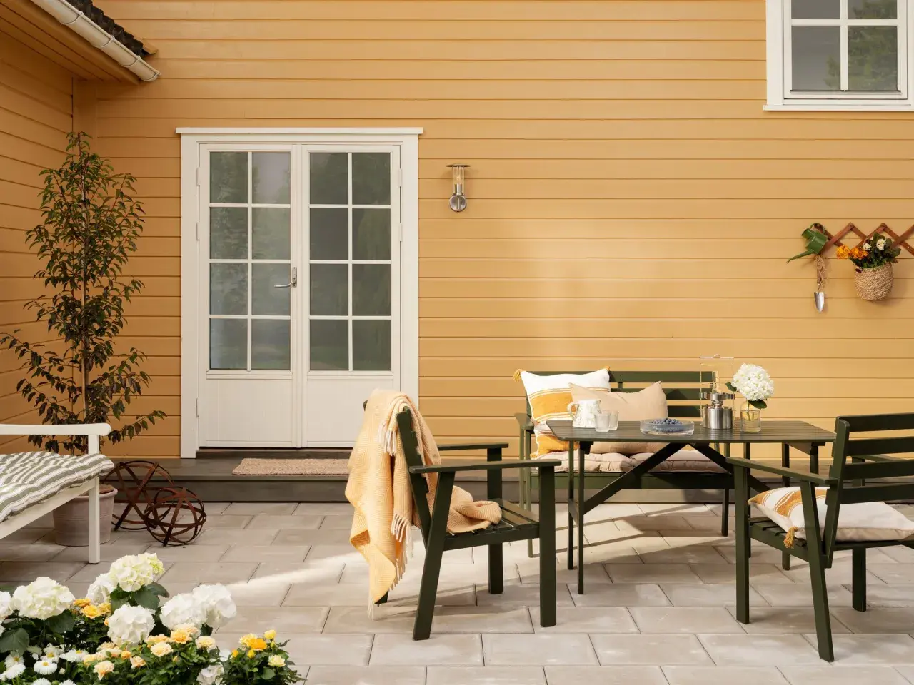 En uteplats med gröna möbler och en gul fasad ger inspiration till ett gult tegelhus. Blommor och en filt skapar en mysig känsla.