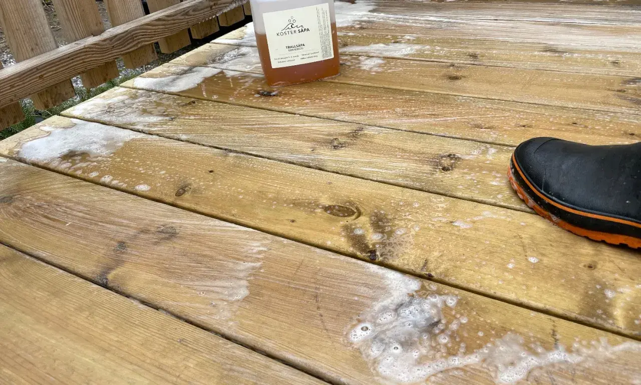 En flaska linoljesåpa står på en altan som håller på att rengöras. En stövel syns i nedre högra hörnet.