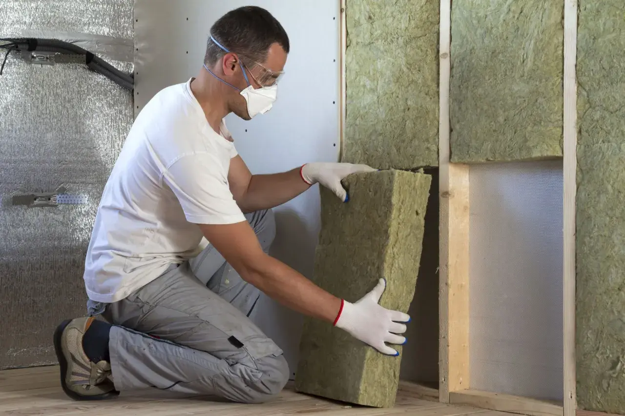 Man med skyddsutrustning installerar tjock isolering i taket.