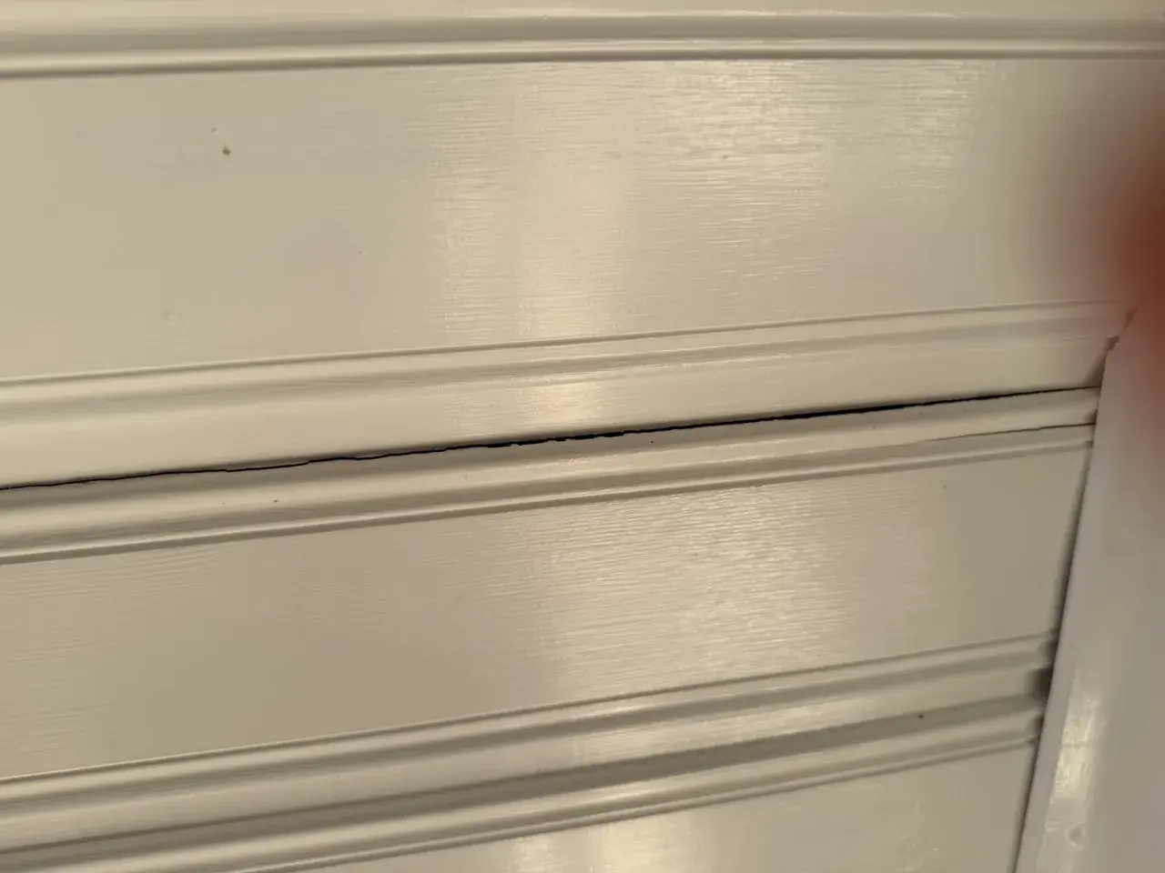 Detaljerad vy av vita träpaneler med synliga sprickor i taket.