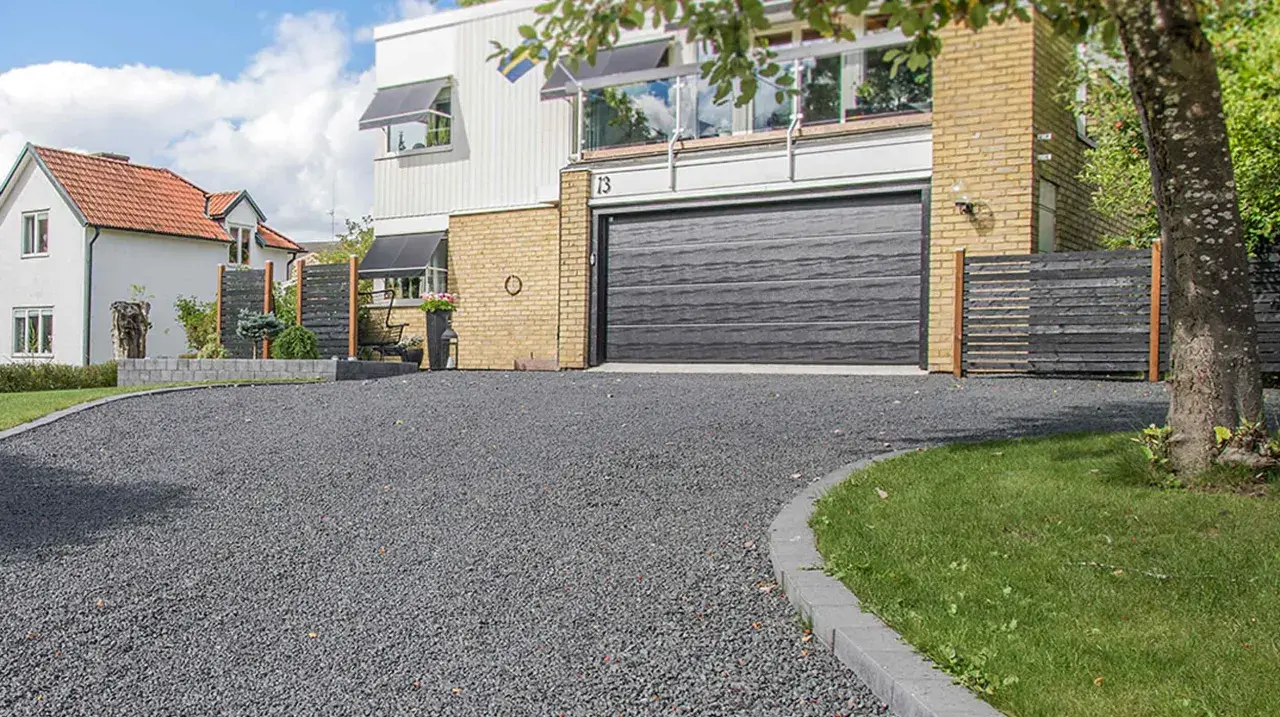 En vacker uppfart med mörkt grus som leder fram till ett modernt hus med garageport.