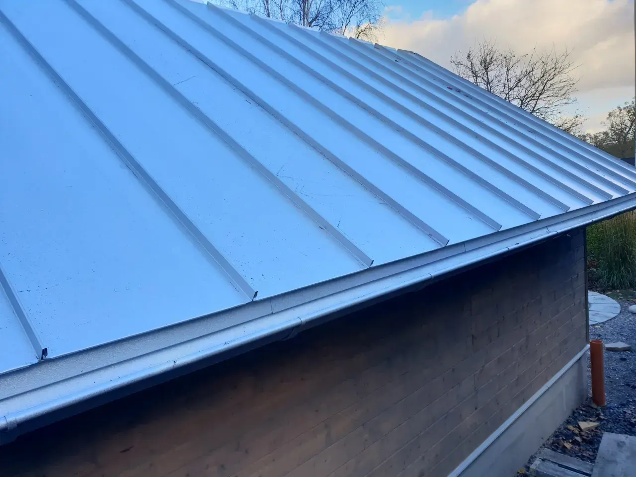 Ett modernt enkelfalsat plåttak på en träfasadbyggnad. Taket är silverfärgat och har en ren, stilren design.