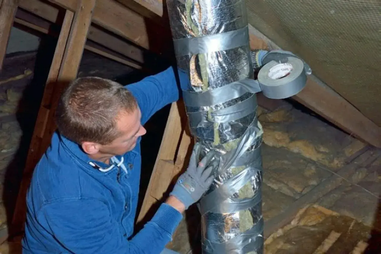 Man tejpar isolerad ventilationskanal i en friggebod.