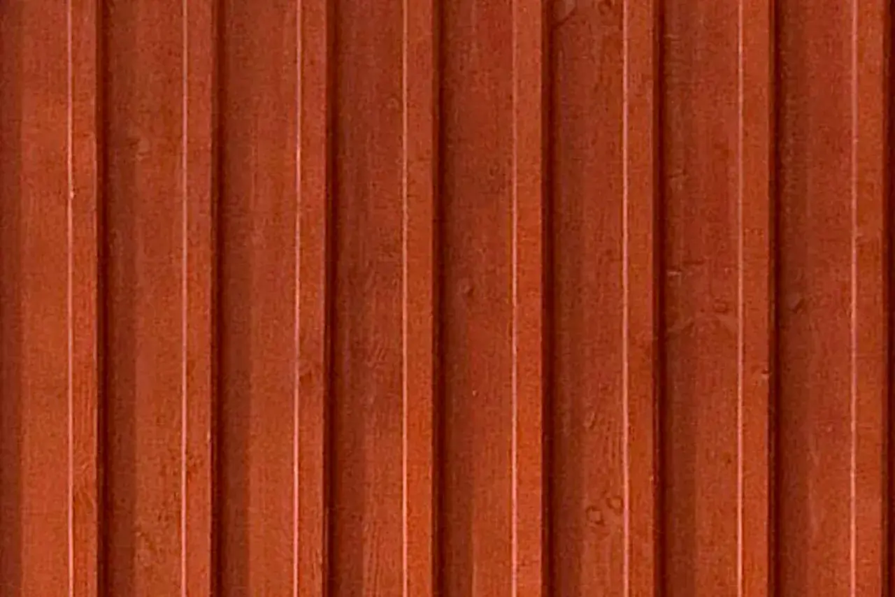 En vägg av gammaldags lockpanel i faluröd färg. Träets ådring syns svagt under färgen.