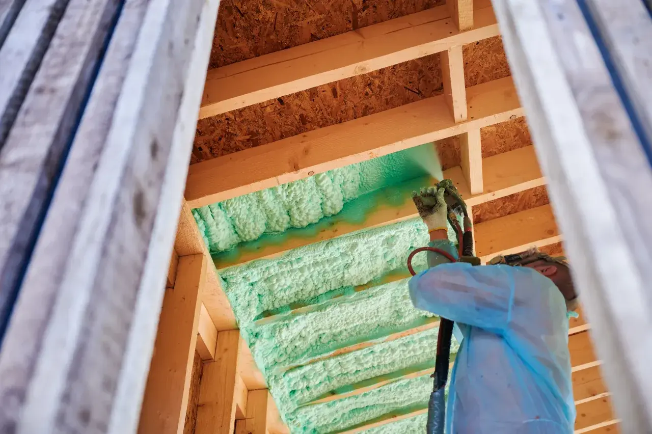 Byggnadsarbetare sprutar grön polyuretanisolering i takbjälkar. Trots dess isolerande fördelar kan polyuretanisolering nackdelar ha gällande miljö och hälsa.