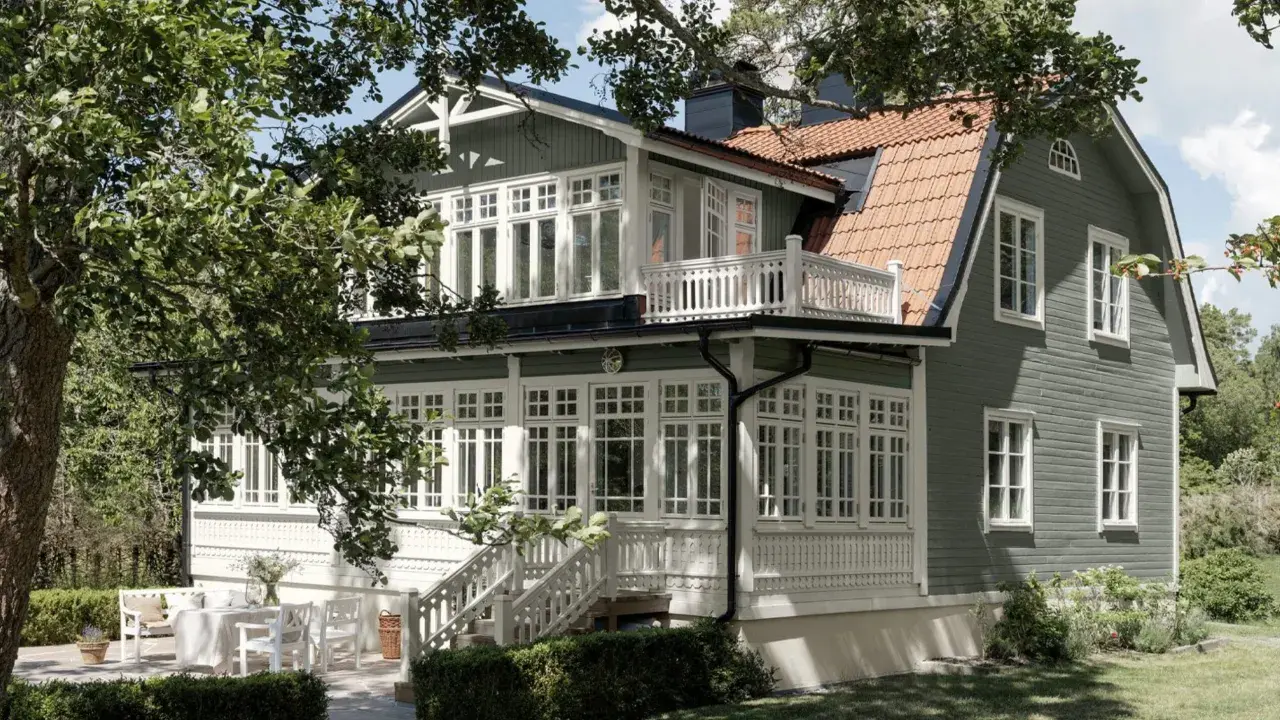 Vackert putsade hus med gröna träfasader och vita detaljer. En veranda med vita möbler och en uteplats inbjuder till avkoppling. Perfekt inspiration för putsade hus.