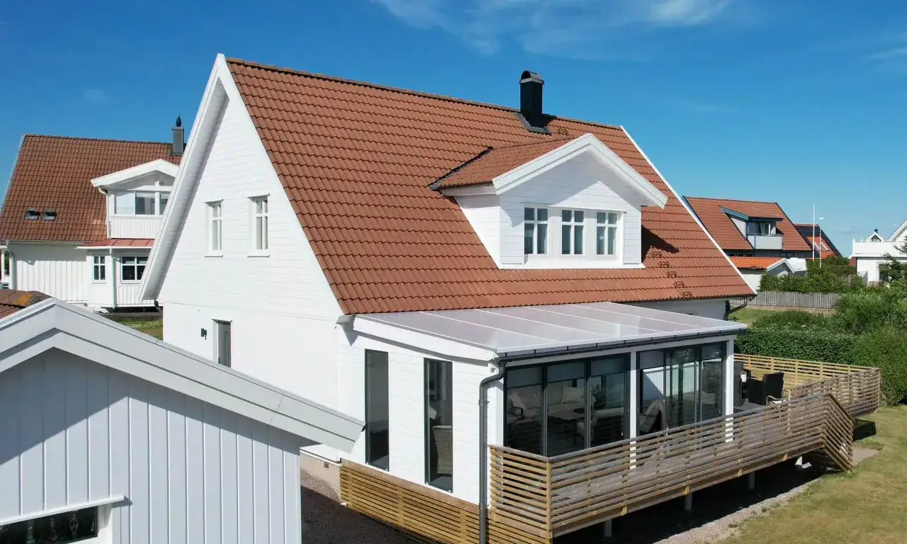 Vitt hus med tegeltak och en takkupa som ger mer ljus. En inglasad veranda och altan.