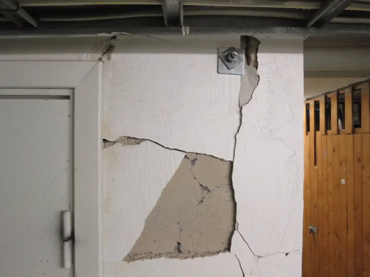 Sprickor i puts fasad visar skador. En metallplatta med bult sitter fast i v&auml;ggen.