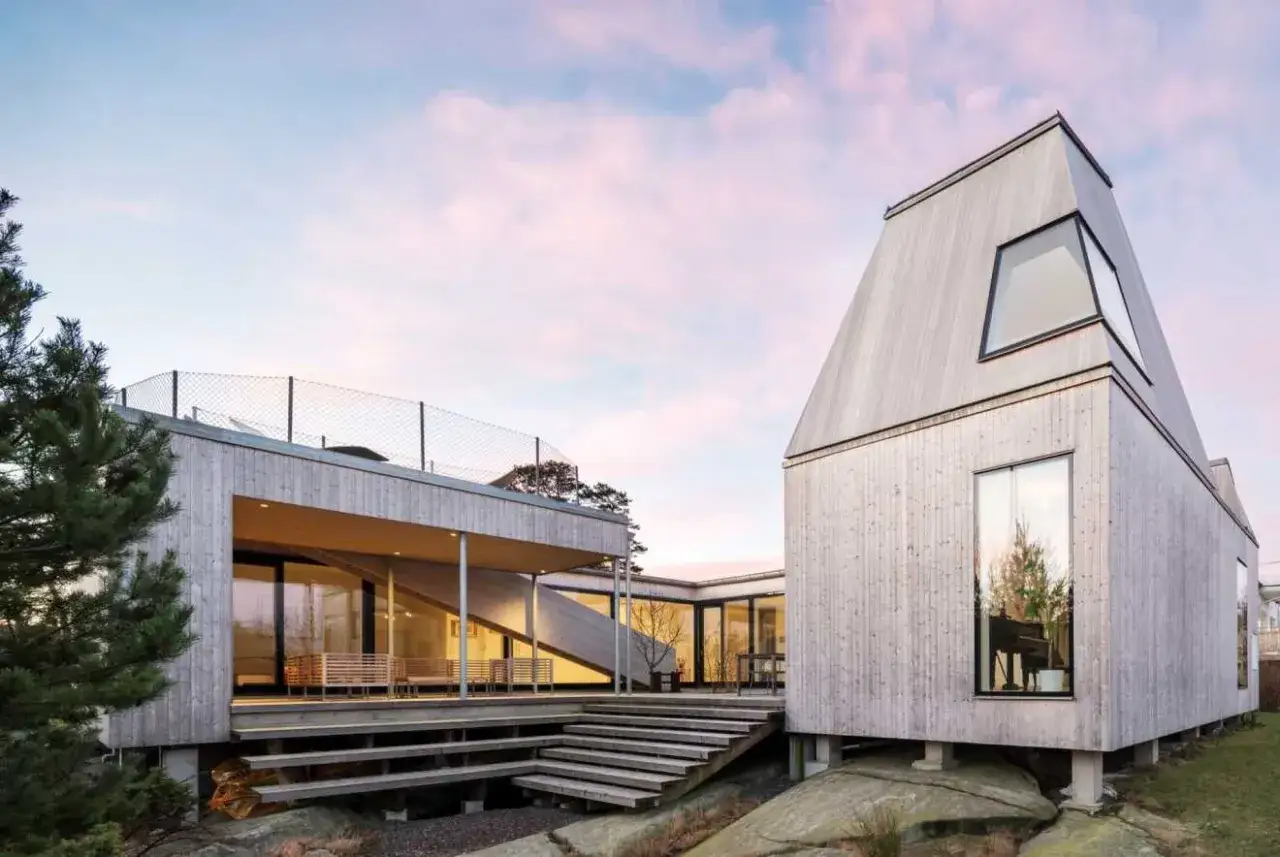 Ett modernt tr&auml;hus med stora f&ouml;nster och en takterrass, ett typiskt Gert Wing&aring;rdh hus, st&aring;r p&aring; klippor vid havet.