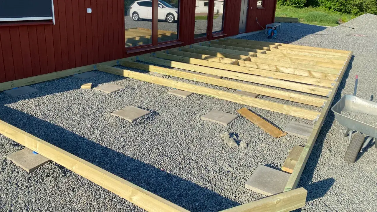 Byggnation av altan med trästomme på grusunderlag. Plattor och plintar syns som stöd.