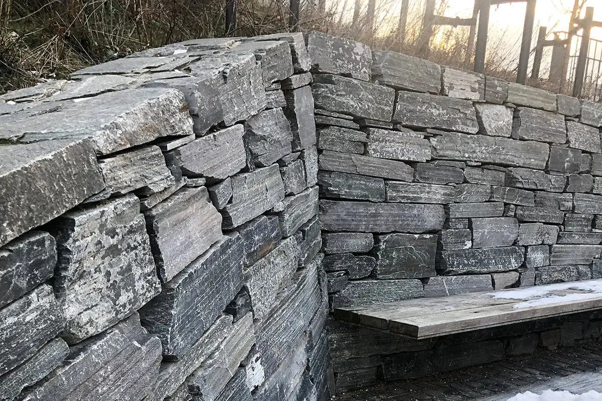 En mur av grovhuggen granit sten, med en enkel tr&auml;b&auml;nk inbyggd.
