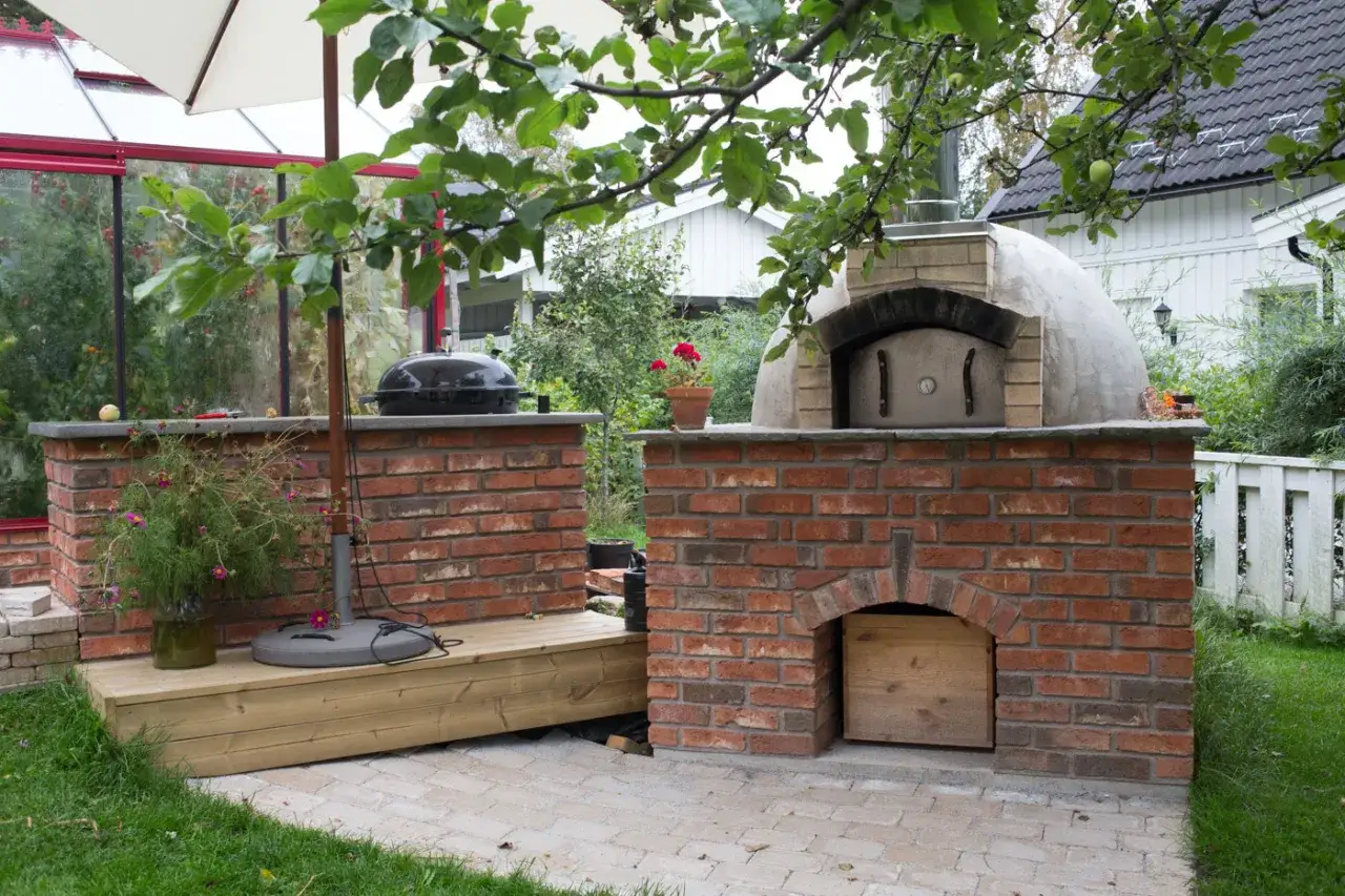 En vacker mura bakugn i tr&auml;dg&aring;rden, redo f&ouml;r pizza. Bredvid st&aring;r en grill och ett v&auml;xthus.
