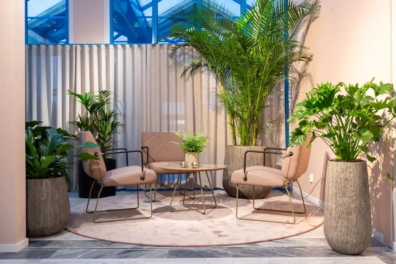 En lugn lounge med antroposofisk inredning, mjuka rosa stolar, ett runt bord och frodiga gr&ouml;na v&auml;xter som skapar en harmonisk oas.