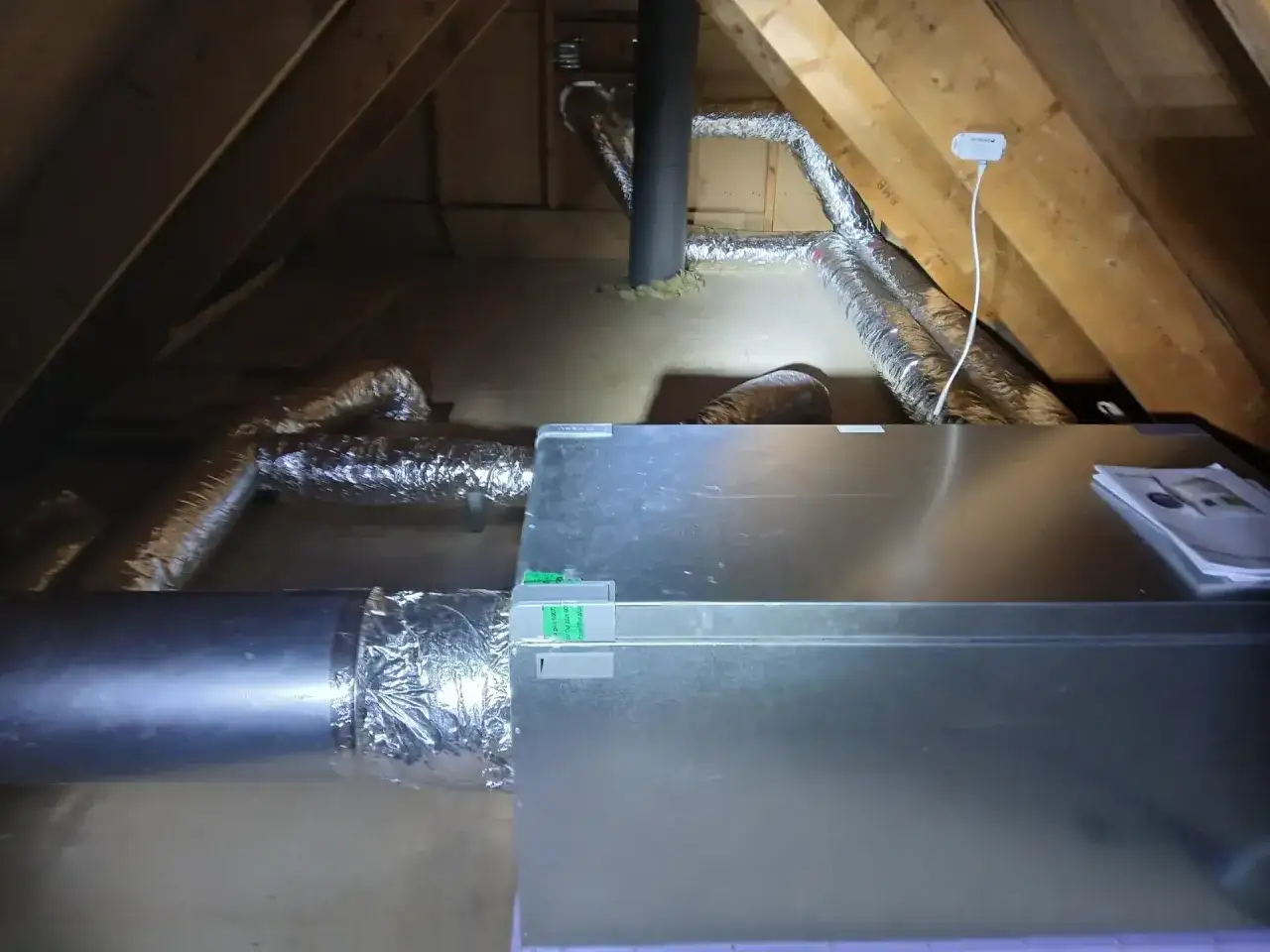 Vindsutrymme med FTX-installation. Flexibla ventilationskanaler och en stor metallenhet syns.