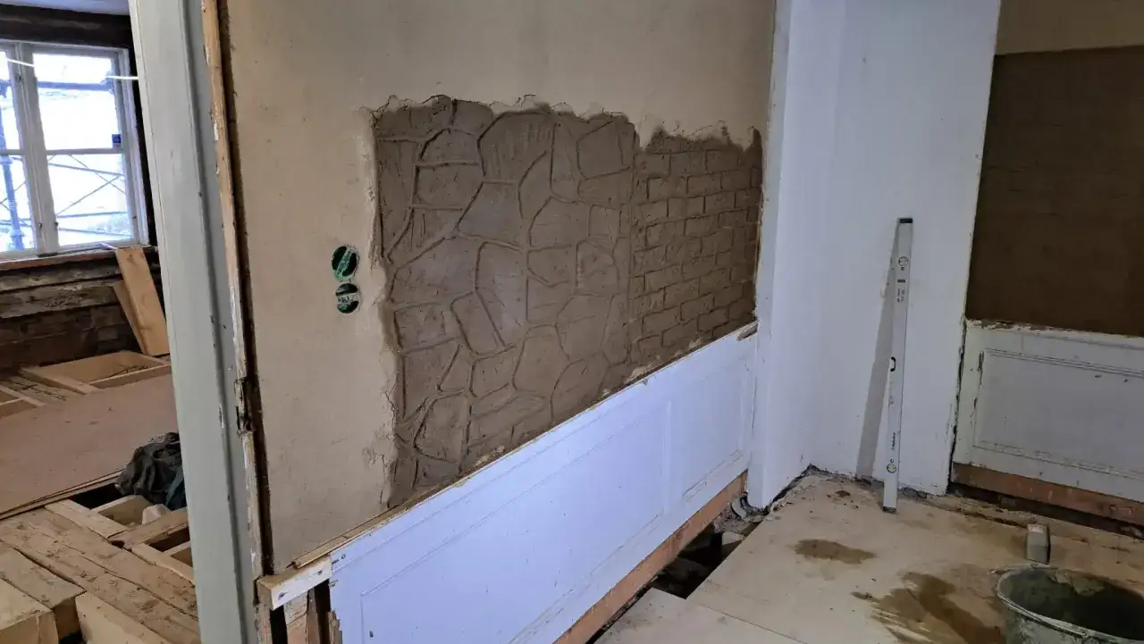 Renovering av v&auml;gg med kalkputs inomhus. En del av v&auml;ggen har en stenliknande textur, en annan liknar tegel.