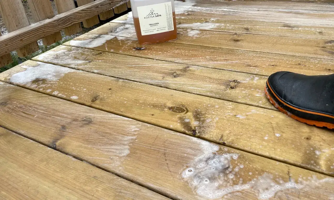 En flaska linoljes&aring;pa st&aring;r p&aring; en altan som h&aring;ller p&aring; att reng&ouml;ras. En svart st&ouml;vel med orange kant syns i nedre h&ouml;gra h&ouml;rnet.