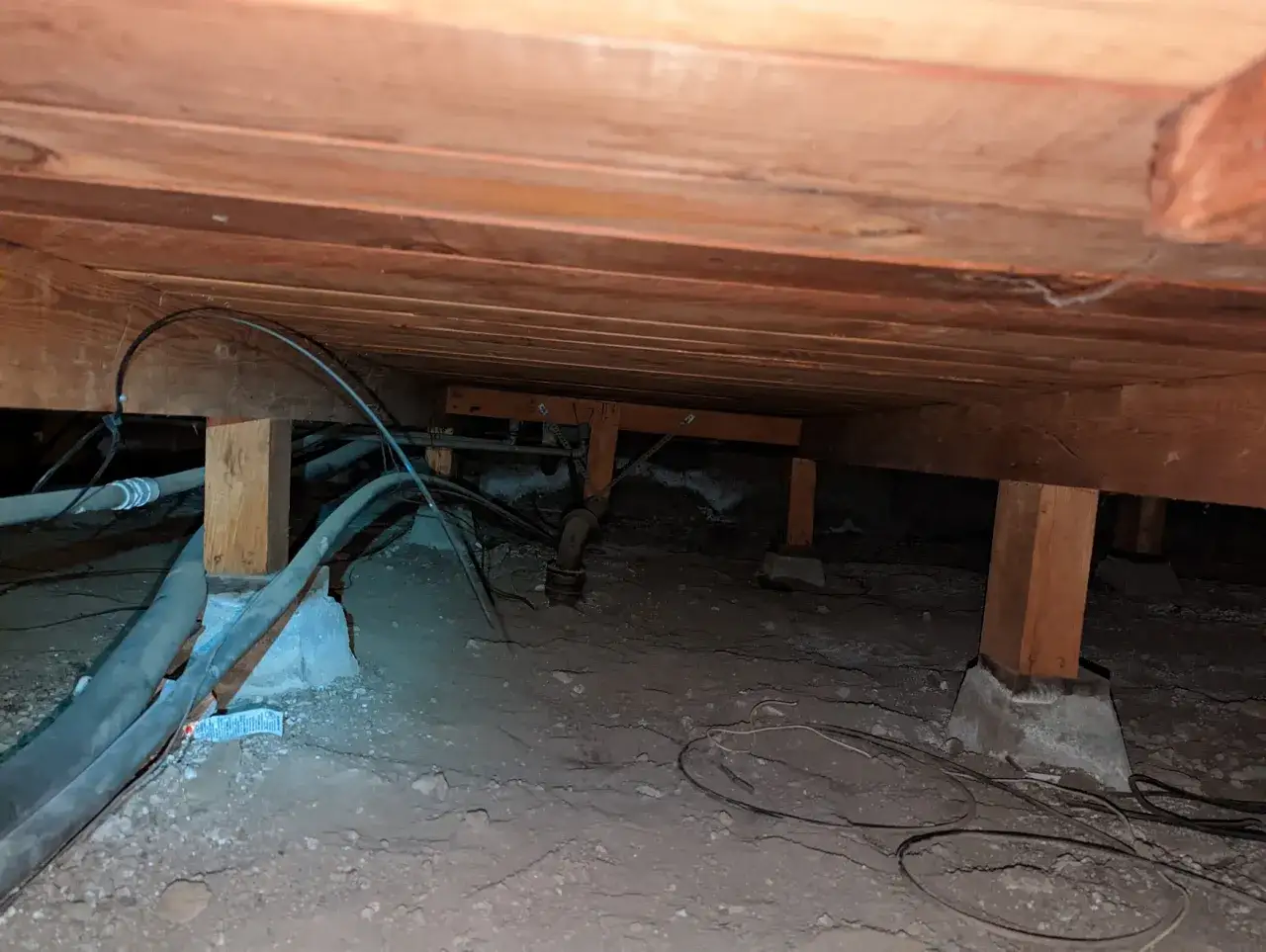 Under golvet syns träbjälkar, rör och kablar. En lösning för att isolera golv utan att bryta upp kan vara att täta utrymmet underifrån.
