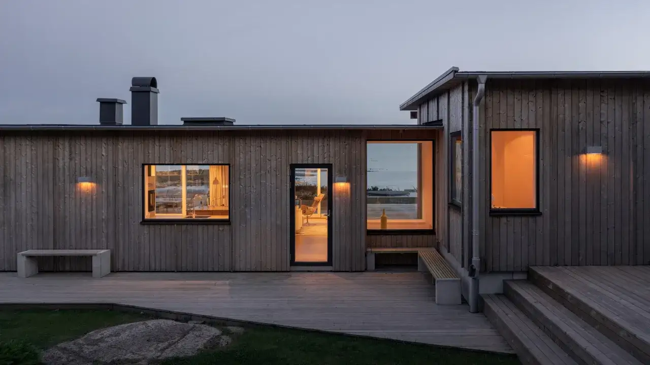 Ett modernt tr&auml;hus med stora f&ouml;nster och en altan. En gul flaska syns i ett f&ouml;nster, som om den v&auml;ntar p&aring; att bli upph&auml;mtad fr&aring;n detta foder hus.